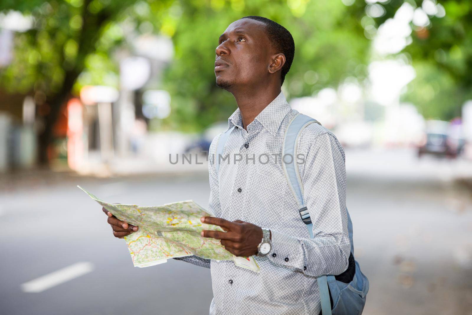 Portrait of a young tourist man looking for his landmarks with a map in town. by vystek