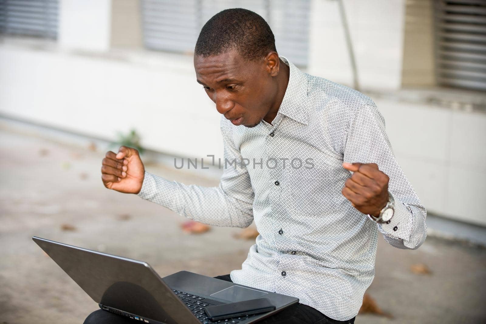 young man sitting in shirt looking at laptop, surprised.