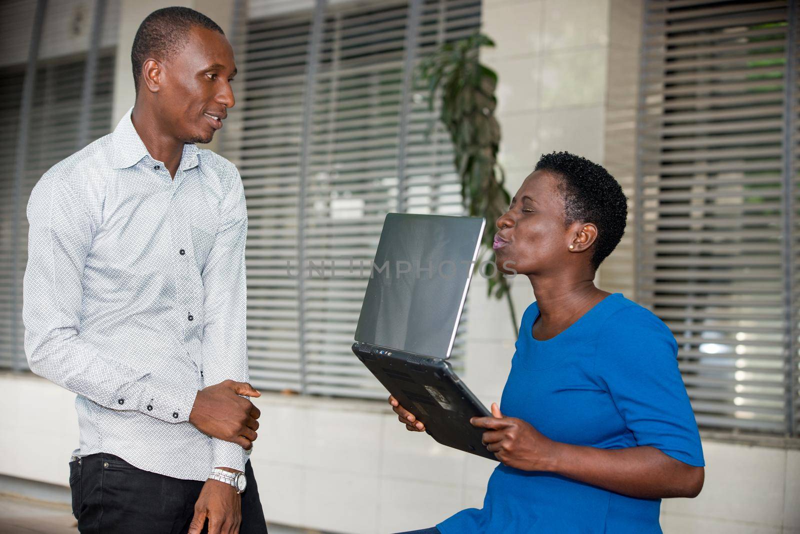 young man standing in shirt looking at his friend kissing computer with eyes closed.