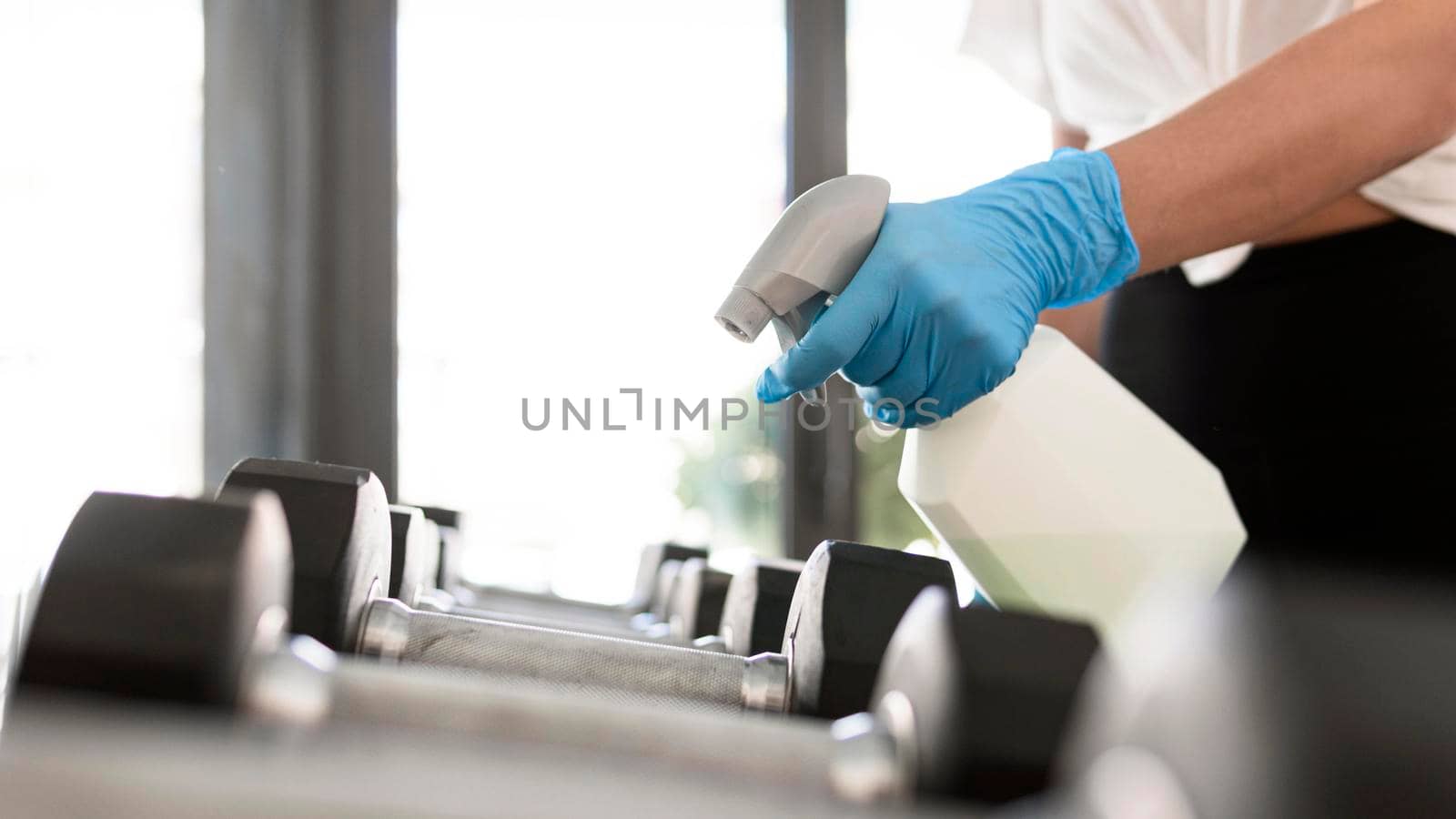 woman with gloves cleaning solution disinfecting gym weights. Beautiful photo