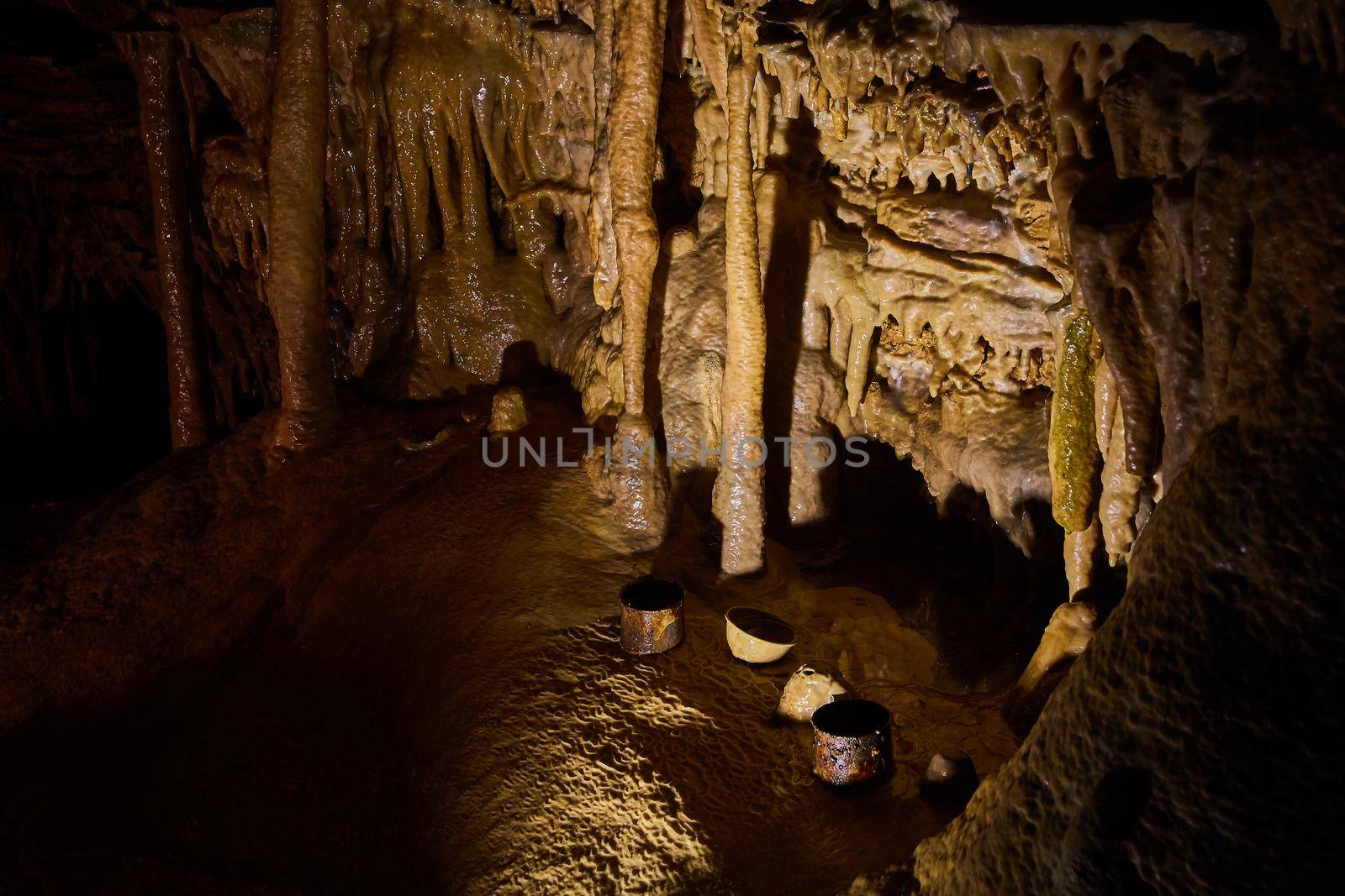 Image of Old drinking cups rusting on ground of deep cave surrounded by stalagmites and stalactites