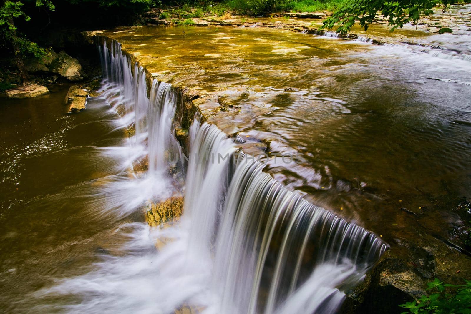 Peaceful waterfalls edge up close flowing into shallow river by njproductions