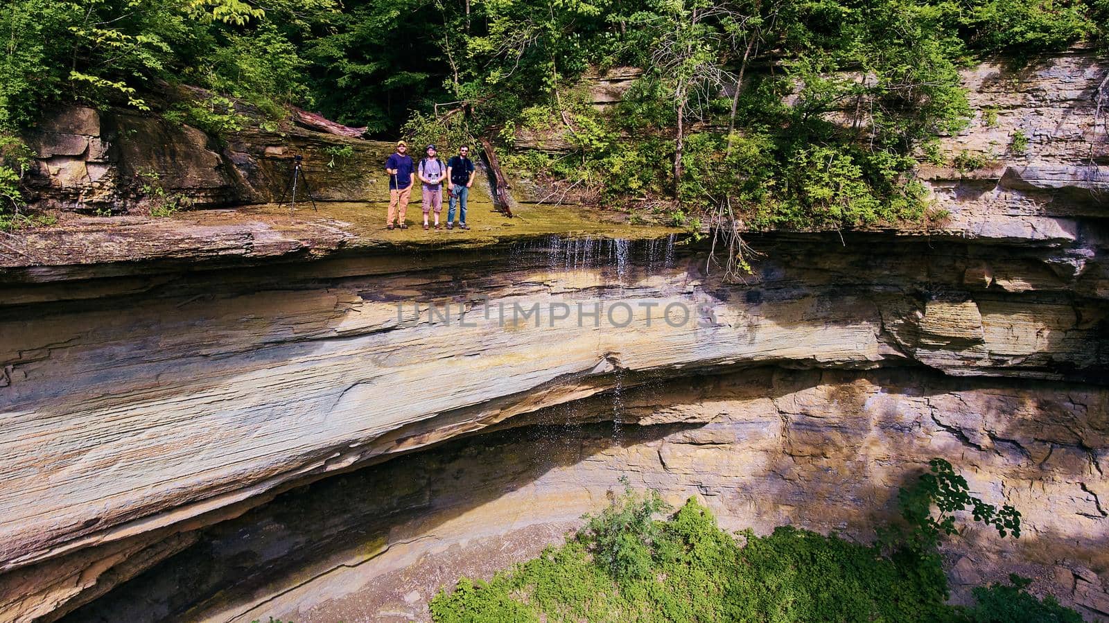 Three figures standing on top of large cliff next to waterfall by njproductions