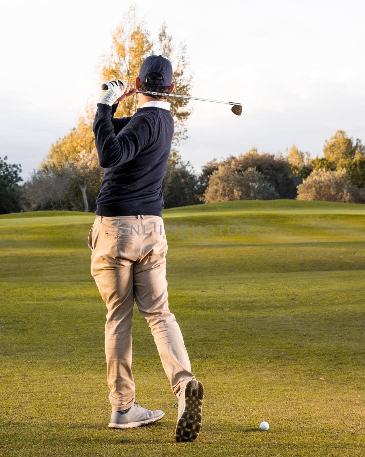 back view man playing grassy golf field. High resolution photo