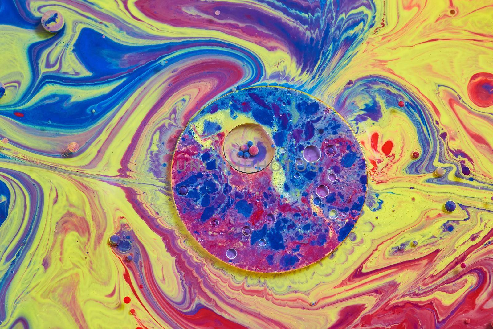 Swirling rainbow colors on surface of liquid with circle patterns and tiny spheres by njproductions