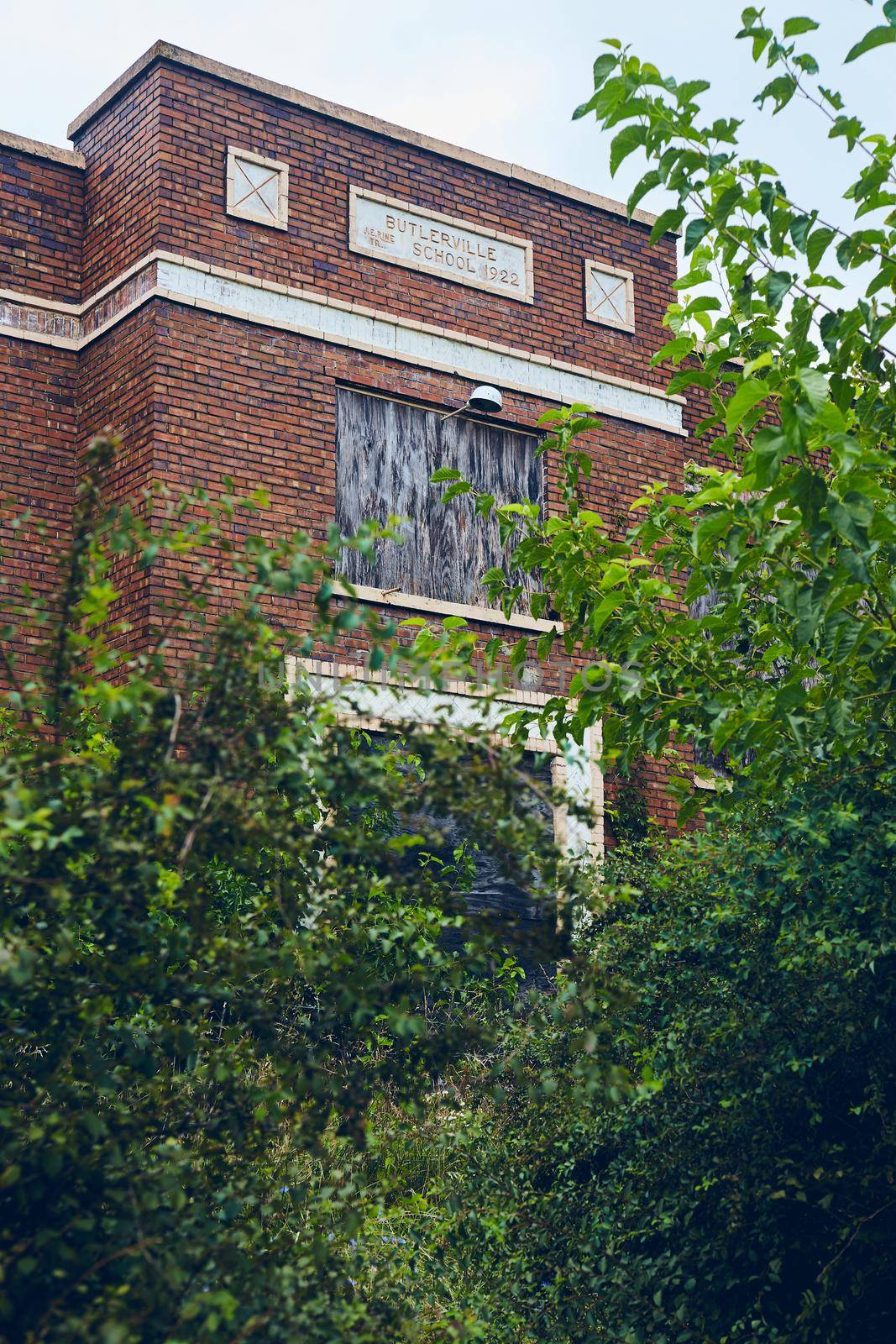Image of Red brick abandoned high school building surrounded by green bushes