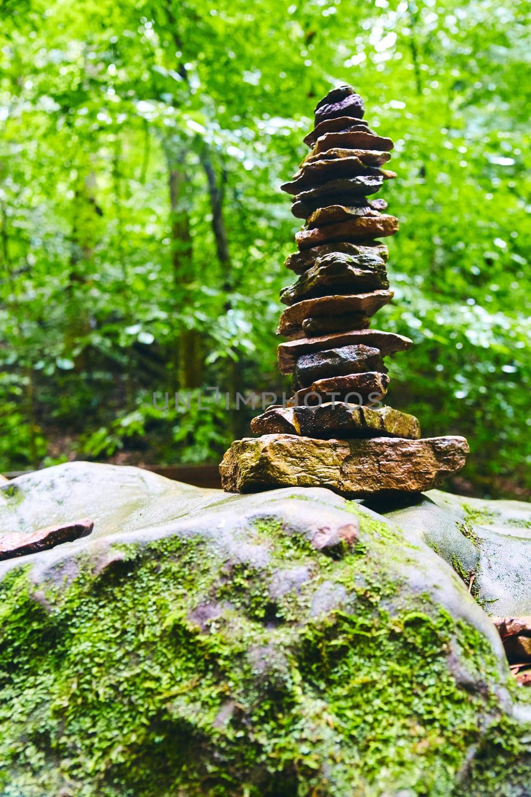 Image of View of tall cairn stack of stones in woods on mossy boulder