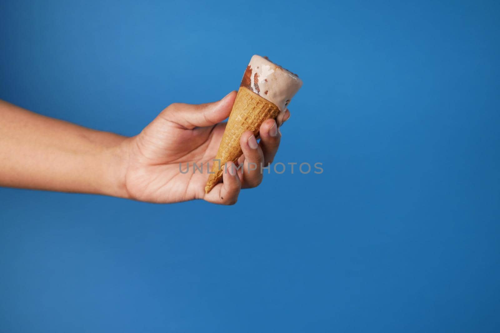 person hand holding ice cream against blue background with copy space by towfiq007