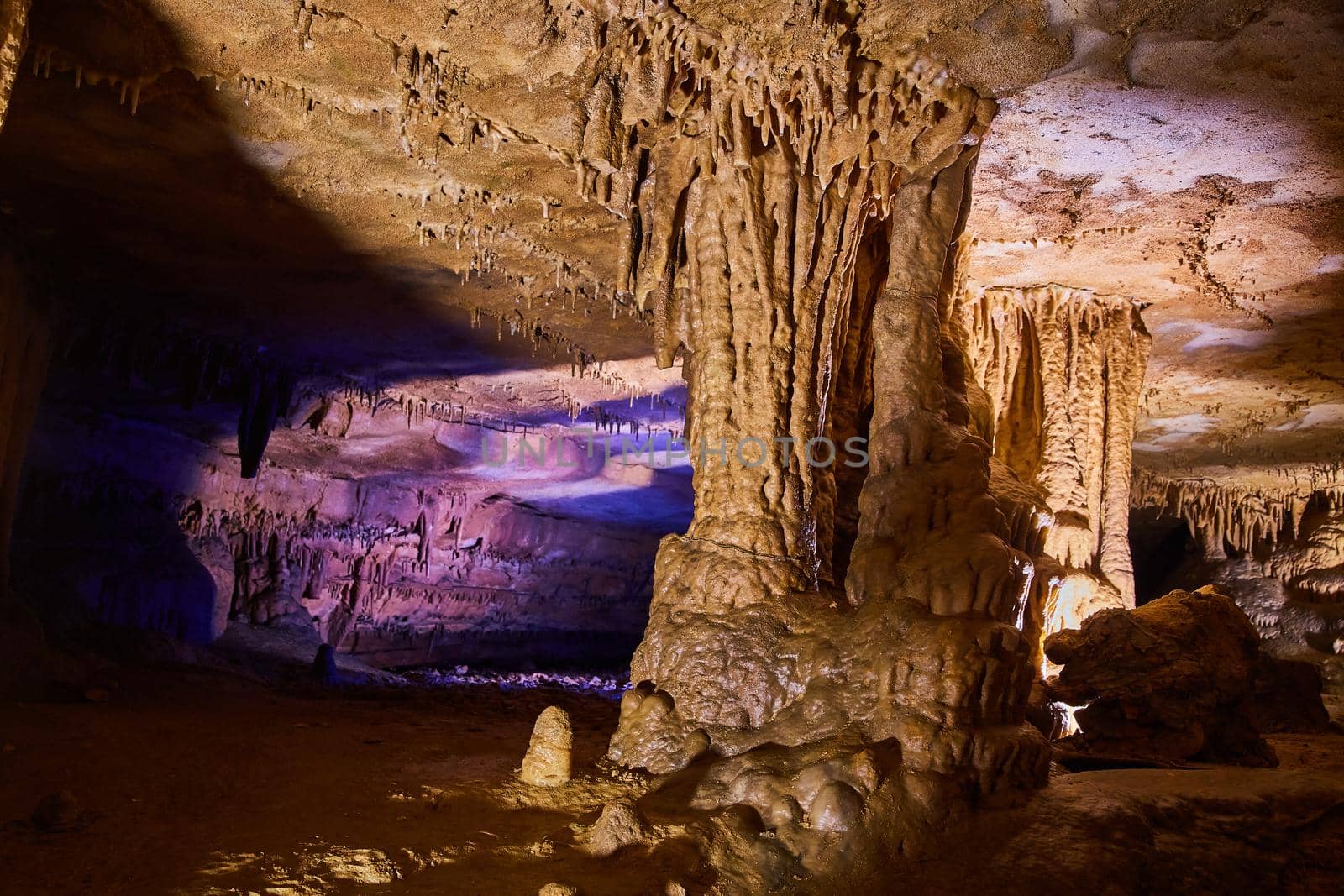 Large rock formations in cave with waxy surface and glow of purple in the background by njproductions