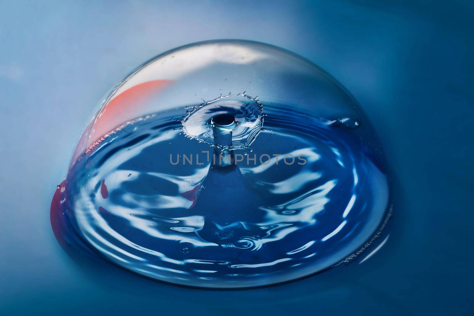 Image of Blue surface with clean bubble containing ripples from two water drops colliding in air