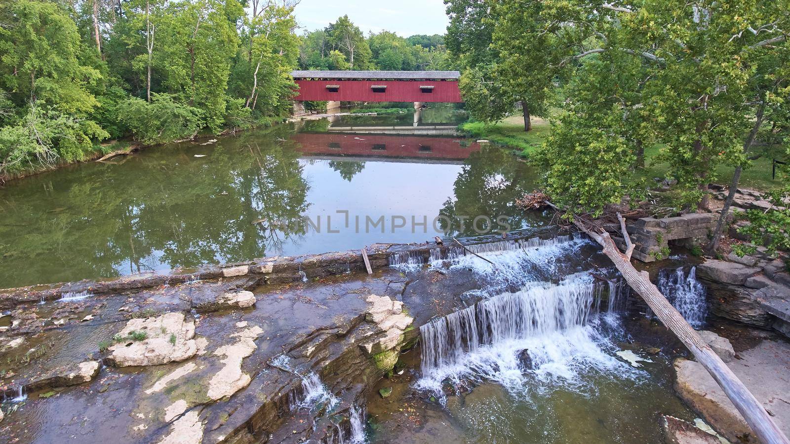 Image of Waterfall at Cataract Falls with a fallen tree collapsed over it and a covered bridge in the background