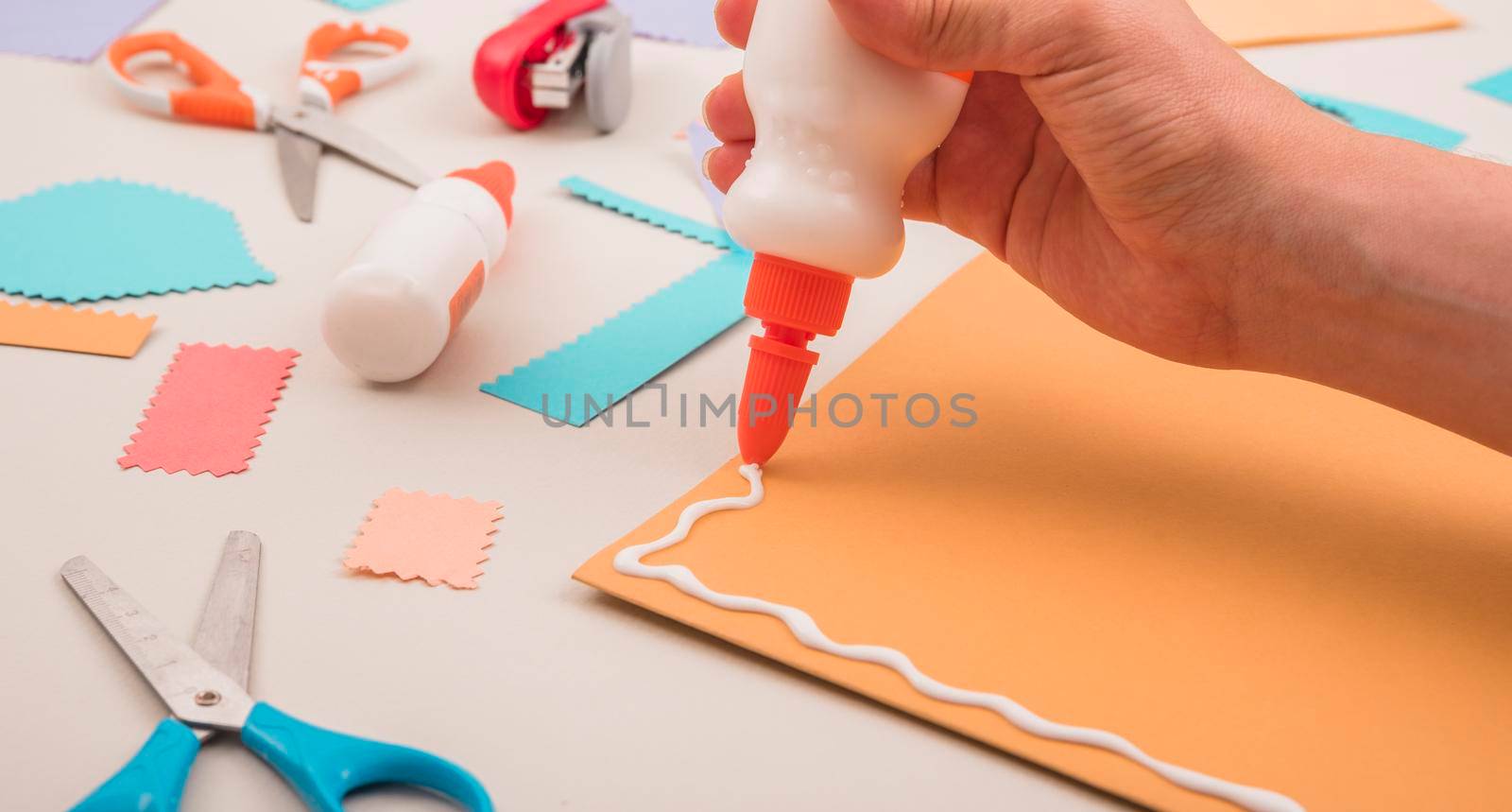 human hand applying white glue orange paper with scissor stapler by Zahard