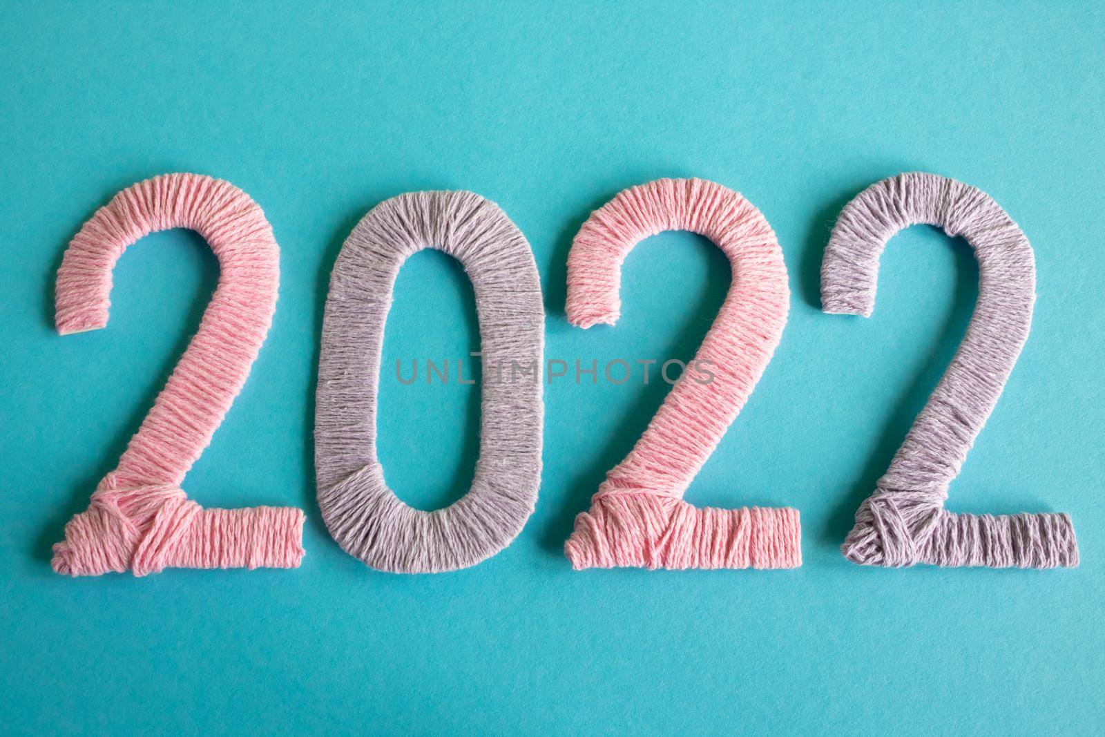 Knitted figures 2022, made of pink and lilac threads, lie on a blue background. The concept of the New Year by lapushka62