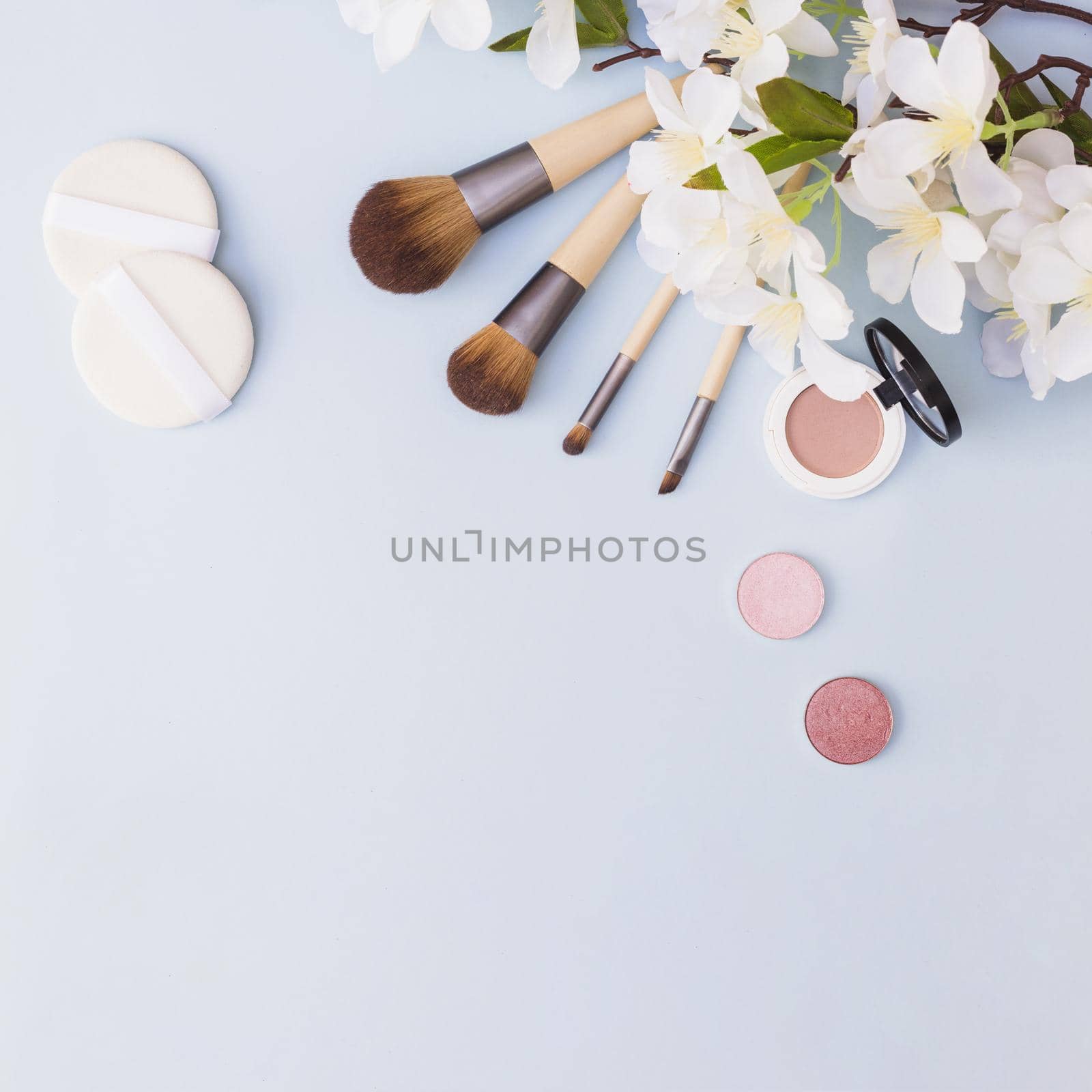 different type makeup brush sponge eye shadow blusher with white flowers blue background. High quality beautiful photo concept by Zahard