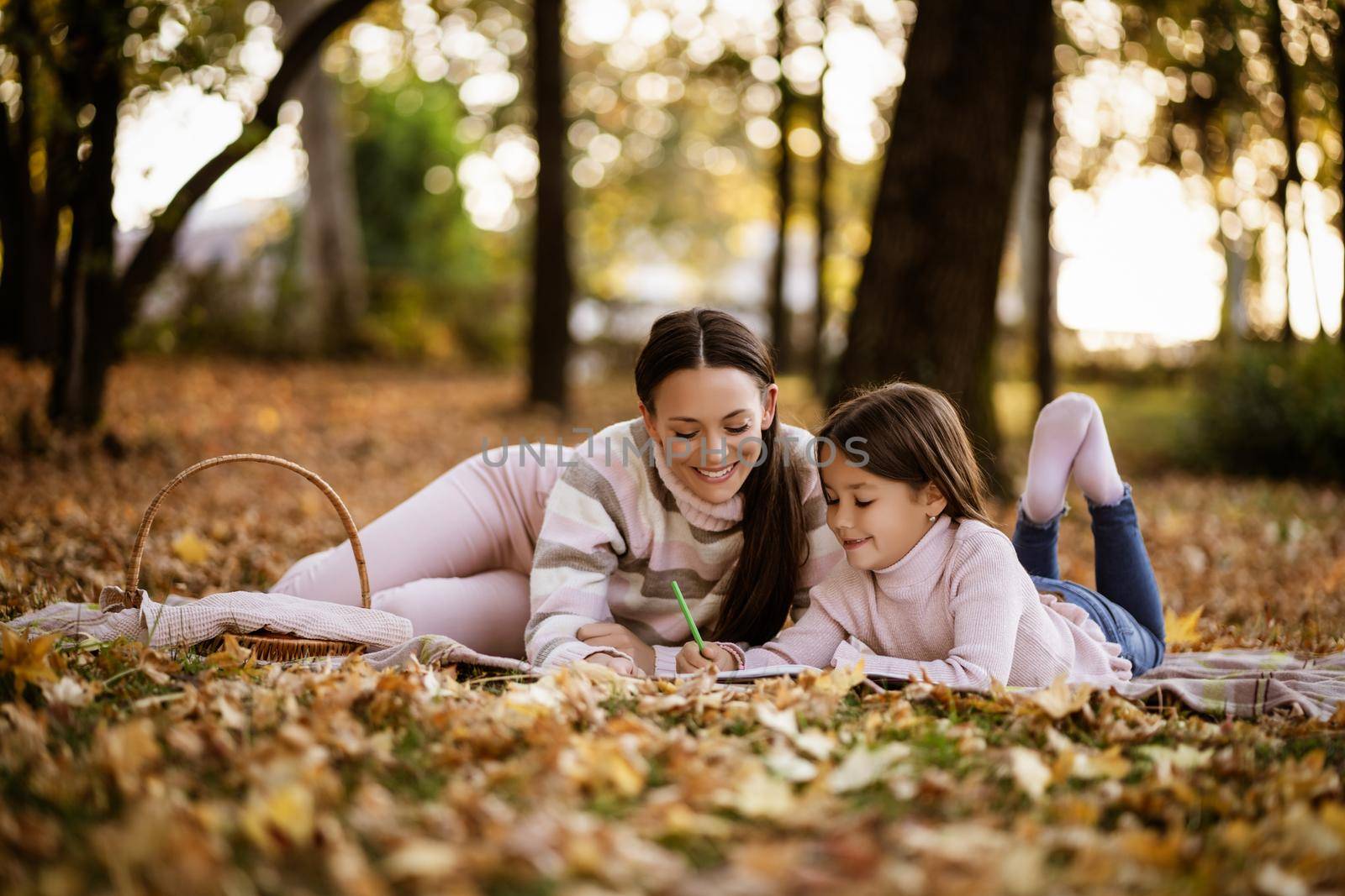 Mother and daughter enjoying autumn in park. Little girl is learning to read.