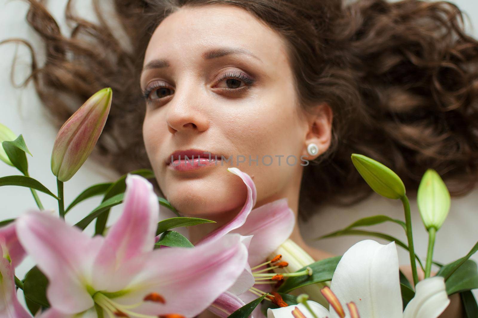 Top view of beautiful woman lying on the table with perfect bouquet of beautiful lilies, female portrait concept.
