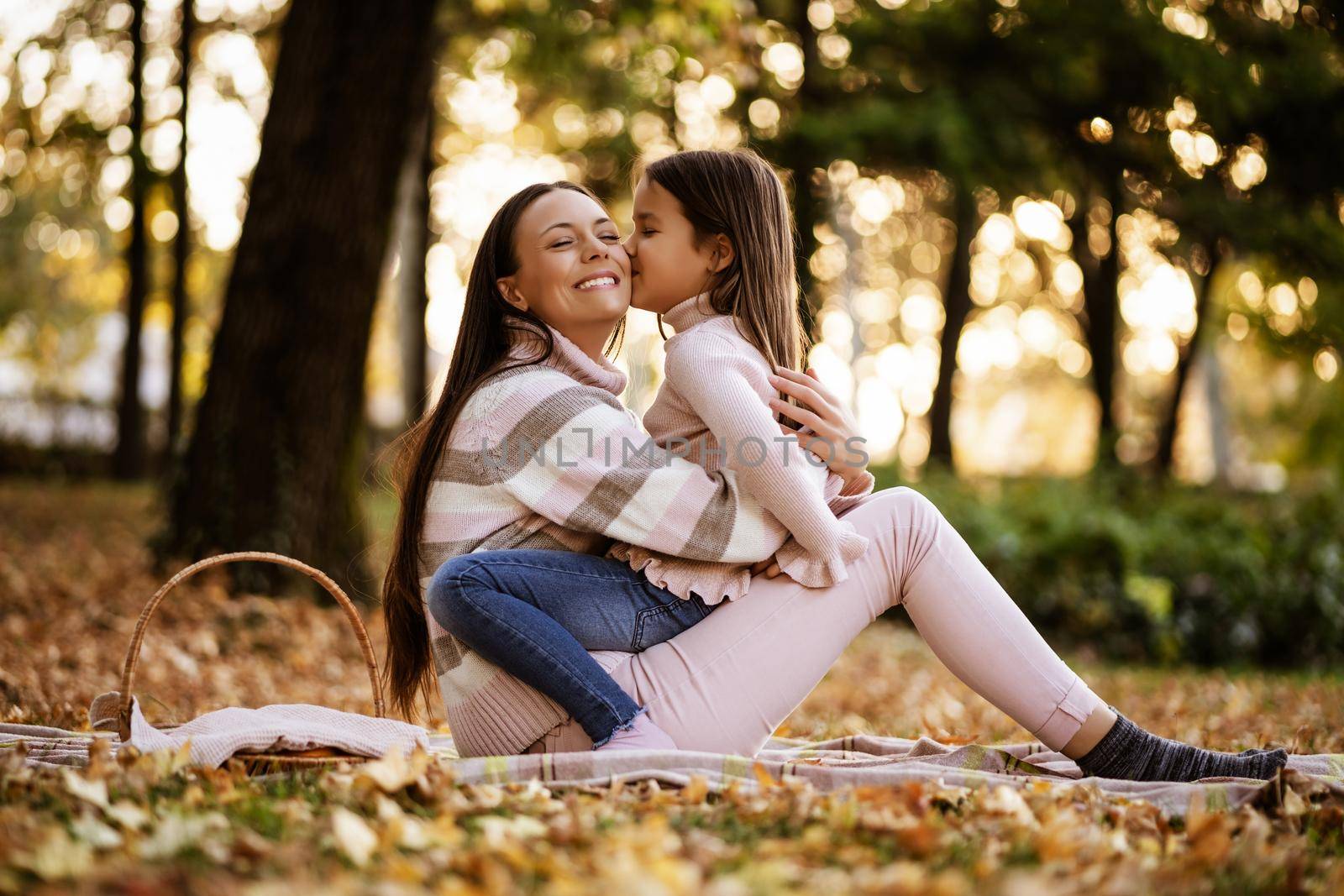 Daughter is kissing her mother in autumn in park.