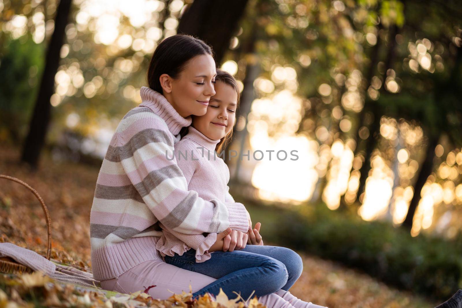 Mother and daughter enjoying autumn in park. They are embracing.