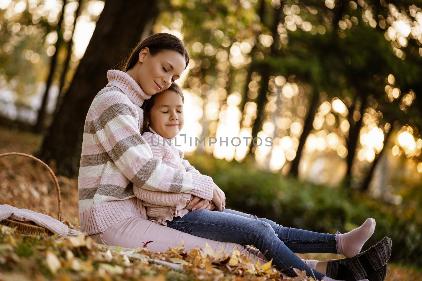 Mother and daughter enjoying autumn in park. They are embracing.