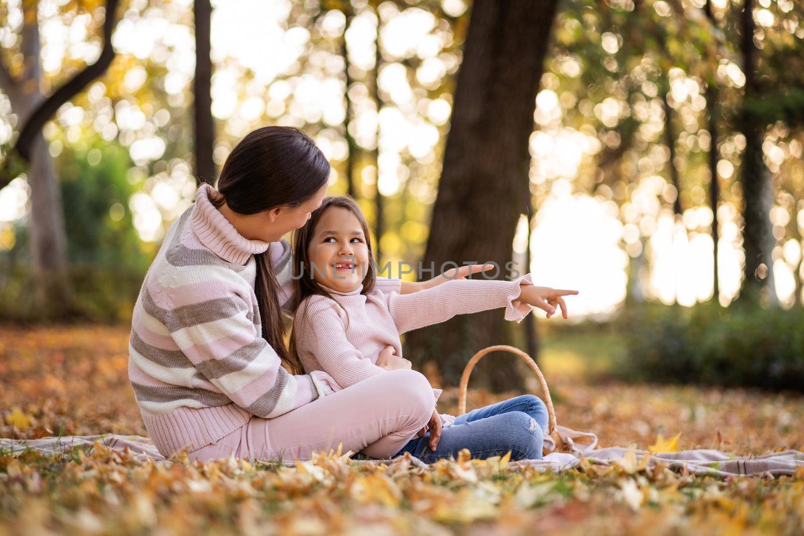 Mother and daughter enjoying autumn in park. Little girl is learning to read.