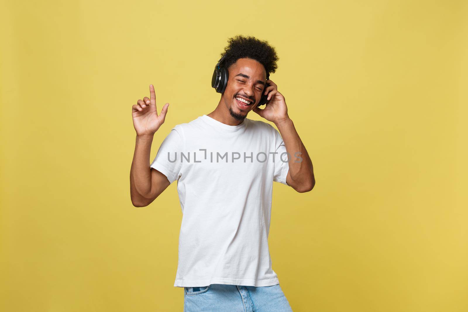Young black man listening to music over his headphones. Isolated over yellow background