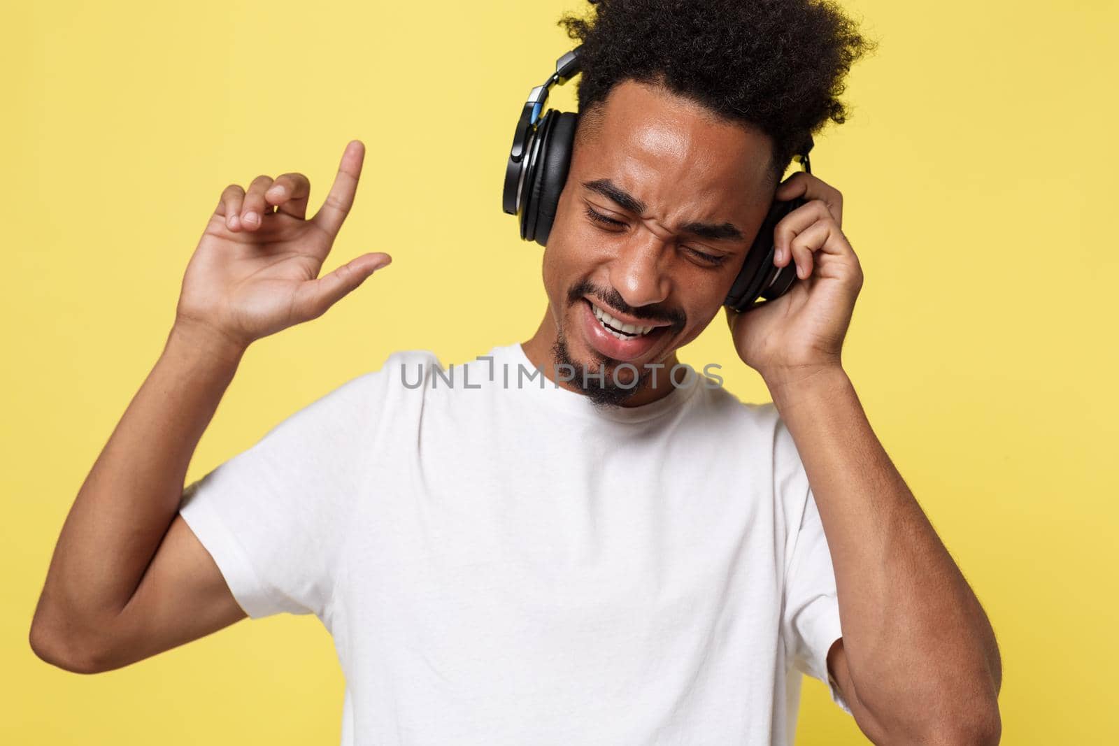 Attractive African American man with headphones listen to music. Isolated over yellow gold background