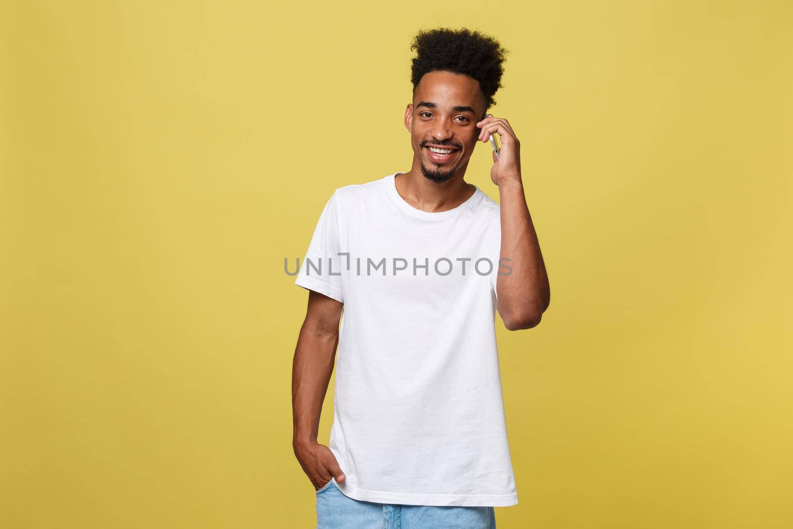 Young black man smiling and talking on mobile phone with copy space over yellow background