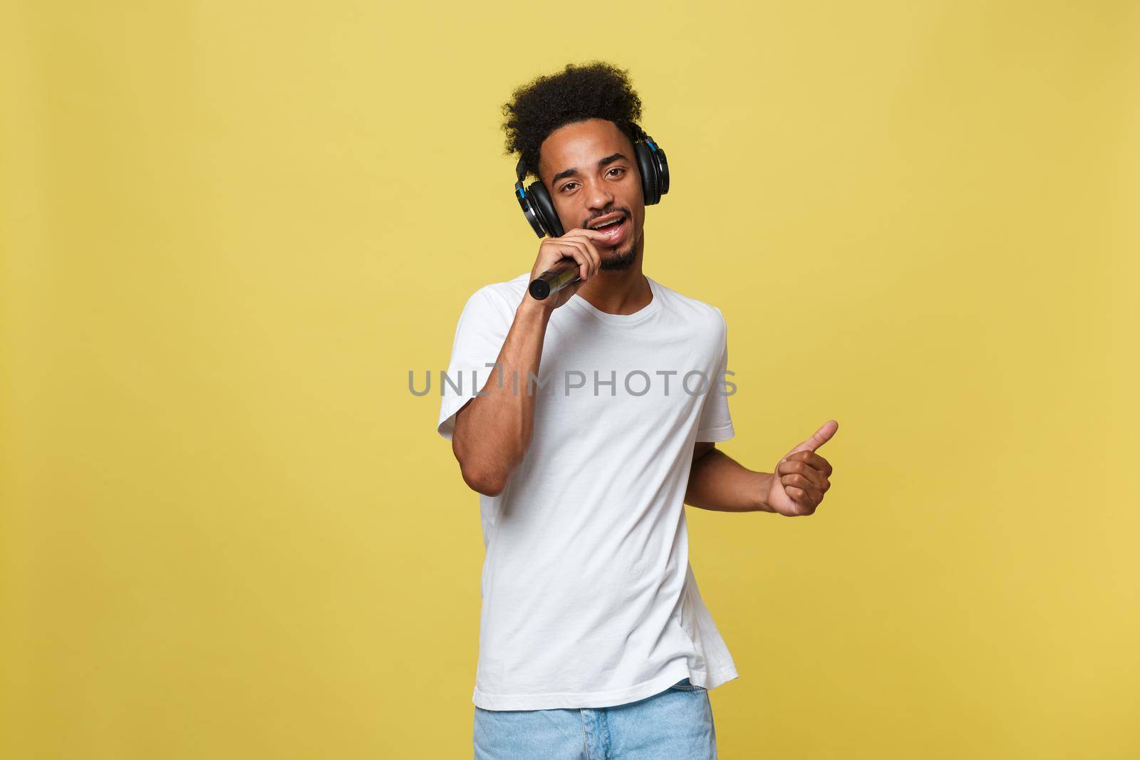 Attractive young dark-skinned man with afro haircut in white t shirt, gesticulating with hands and microphone, dancing and singing on party, having fun