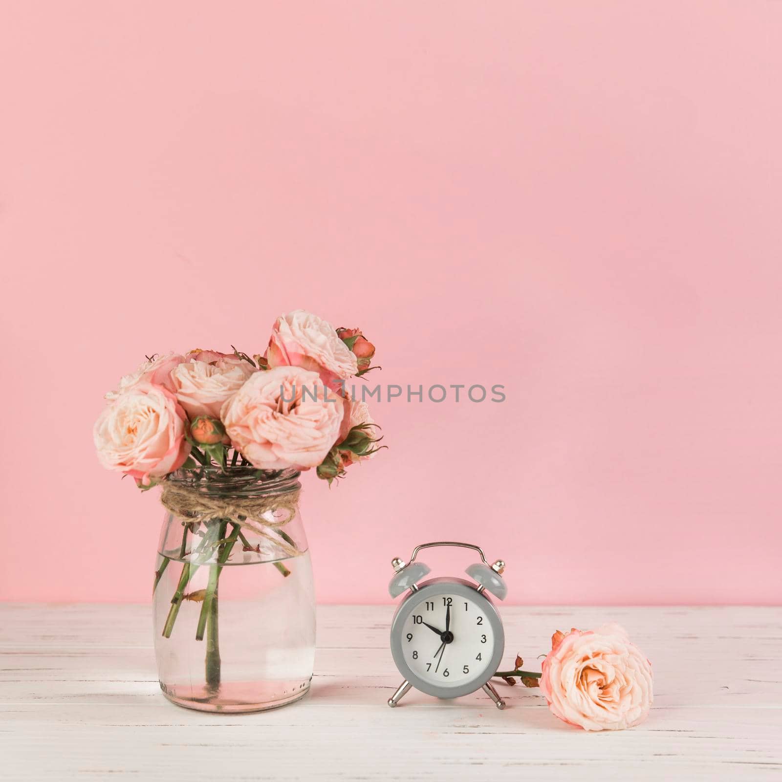 roses vase near alarm clock wooden desk against pink background. High quality photo by Zahard