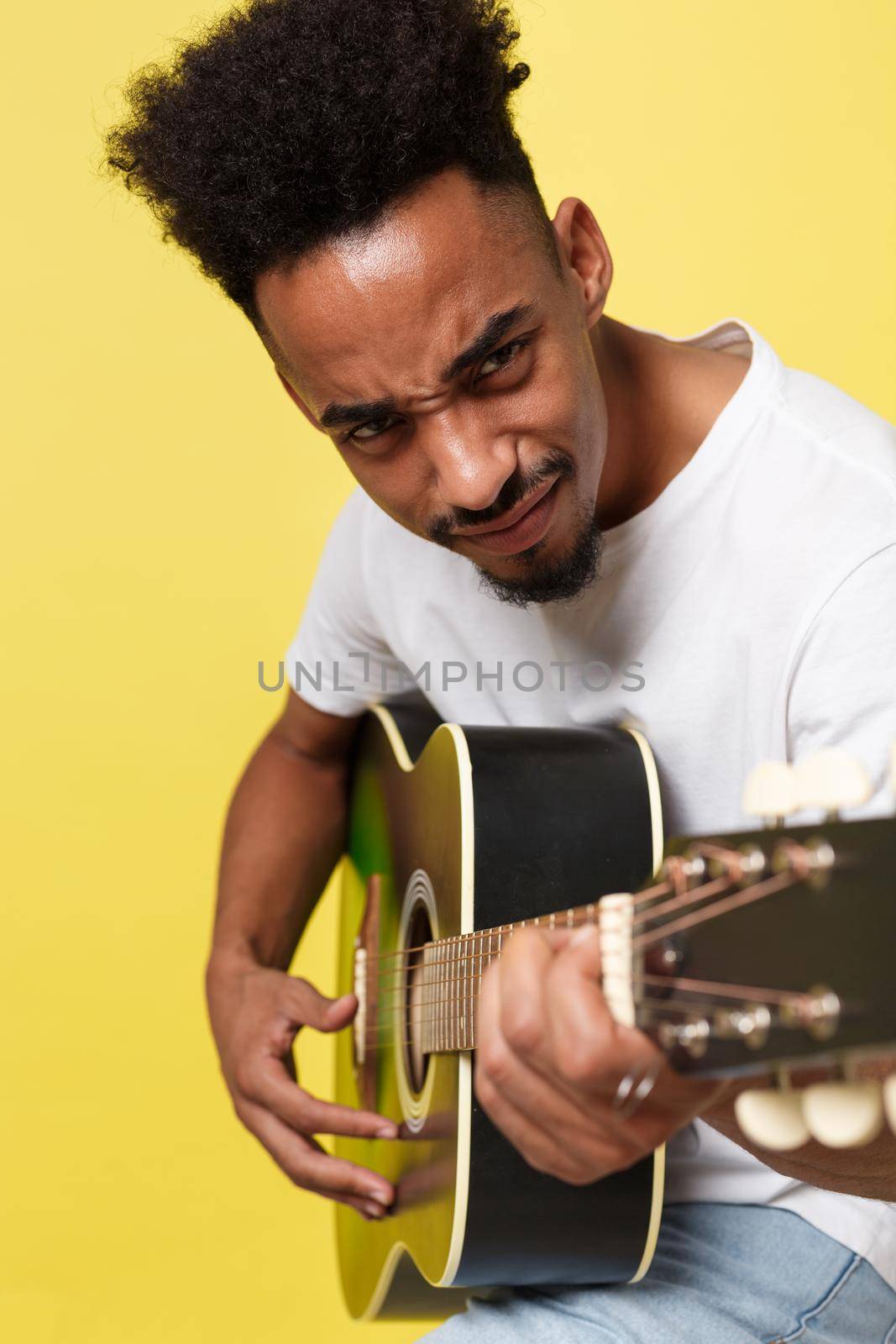 Young handsome African American retro styled guitarist playing acoustic guitar isolated on yellow gold background. by Benzoix