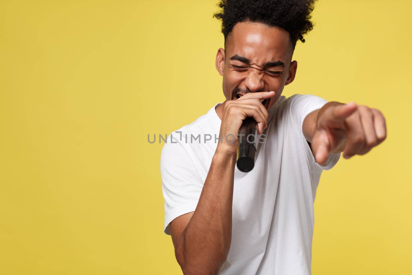 Stylish afro american man singing into microphone isolated on a yellow gold background.