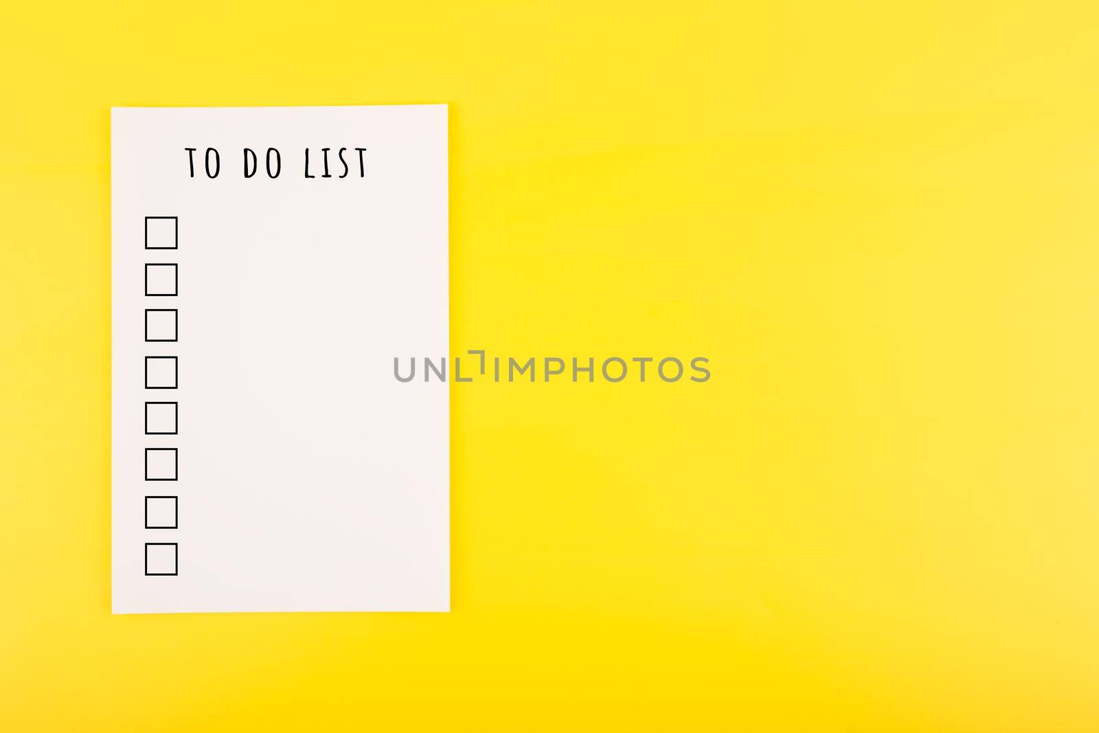 To do list concept in bright yellow color with copy space. White sheet of paper with to do list headline and checkboxes on yellow background with copy space