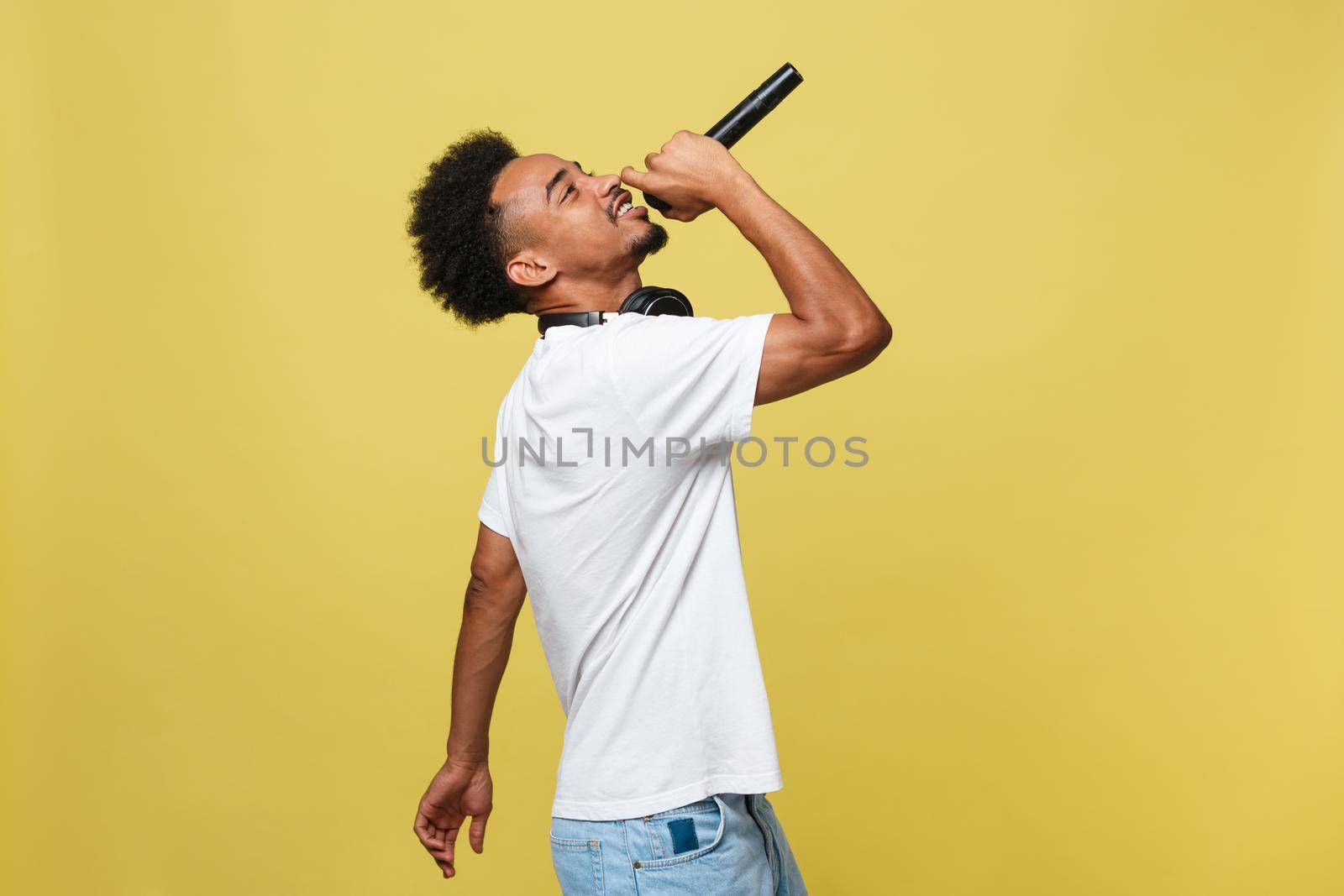 Young handsome African American Male Singer Performing with Microphone. Isolated over yellow gold background. by Benzoix