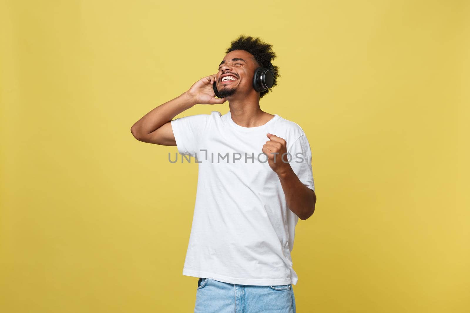 Young African American man wearing headphone and enjoy music over yellow gold Background by Benzoix