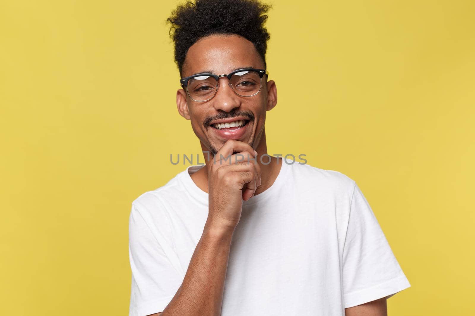 Headshot of good-looking positive young dark-skinned male with stubble and trendy haircut wearing white shirt while posing isolated against blank studio wall background with copy space for your text.