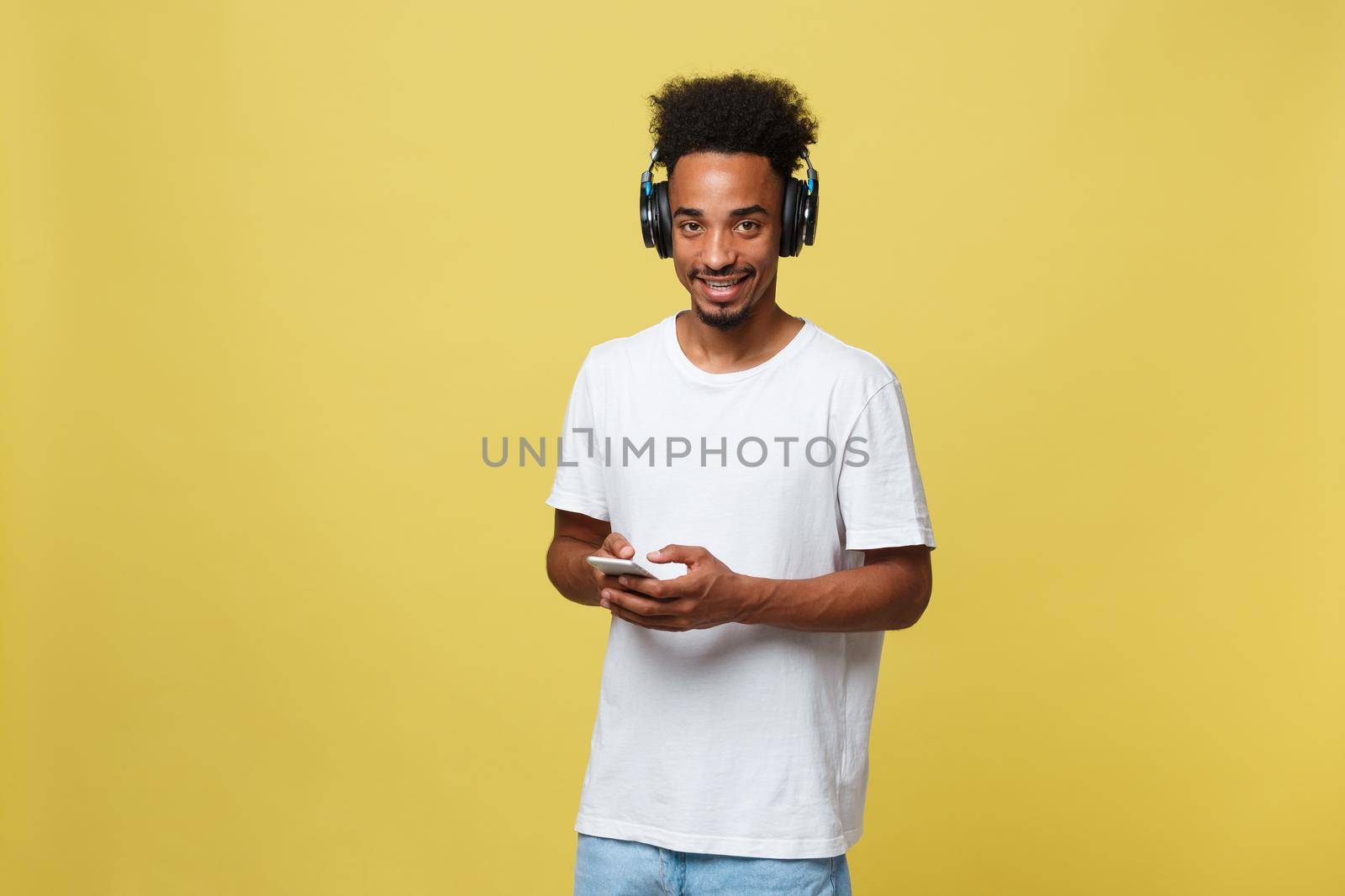 Young black man listening to music over his headphones. Isolated over yellow background. by Benzoix