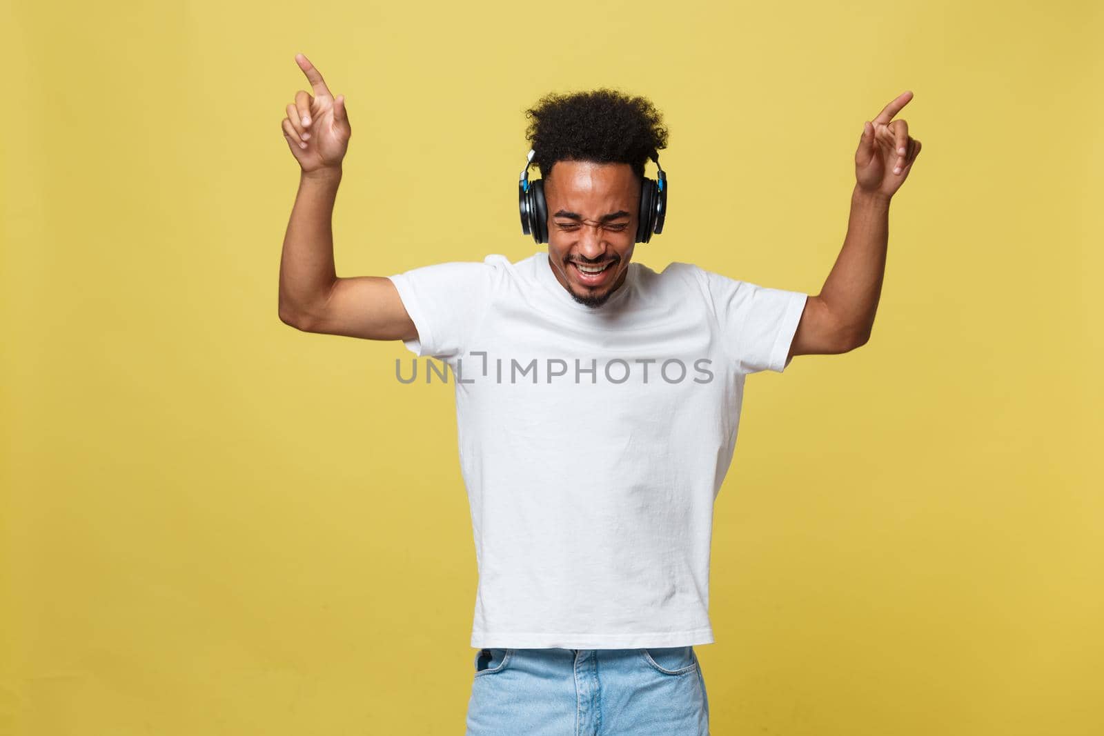 Young African American man wearing headphone and enjoy music over yellow gold Background.