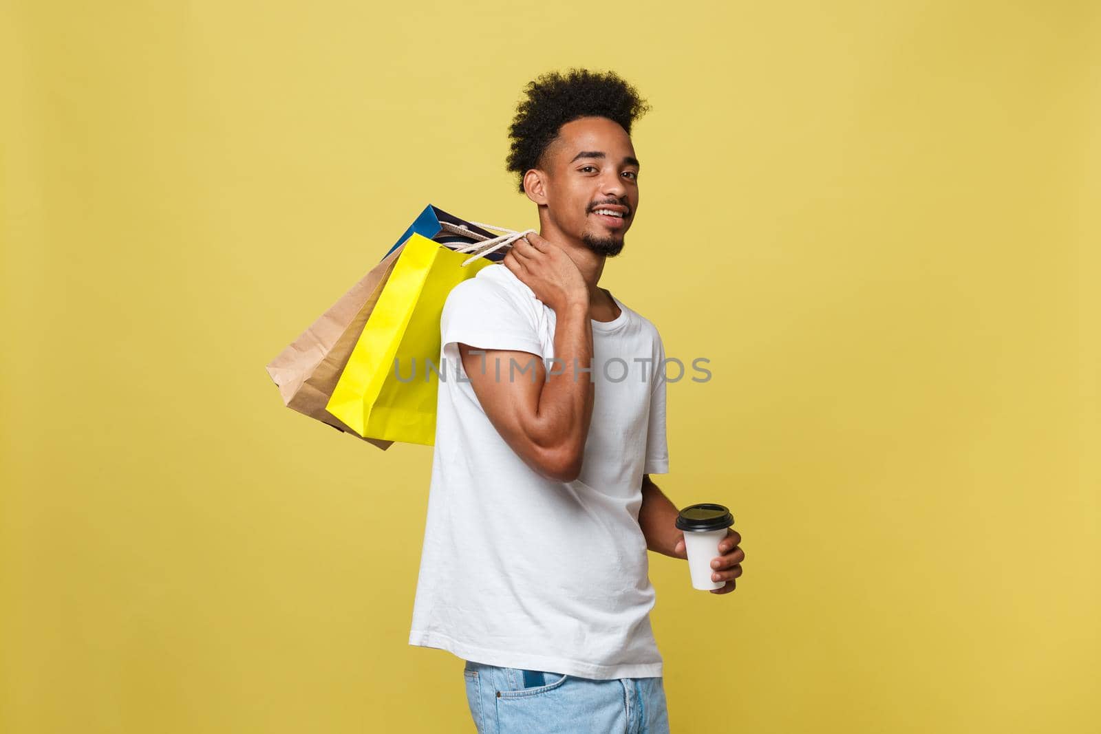 Handsome African American with shopping bag and take away coffee cup. Isolated over yellow gold background