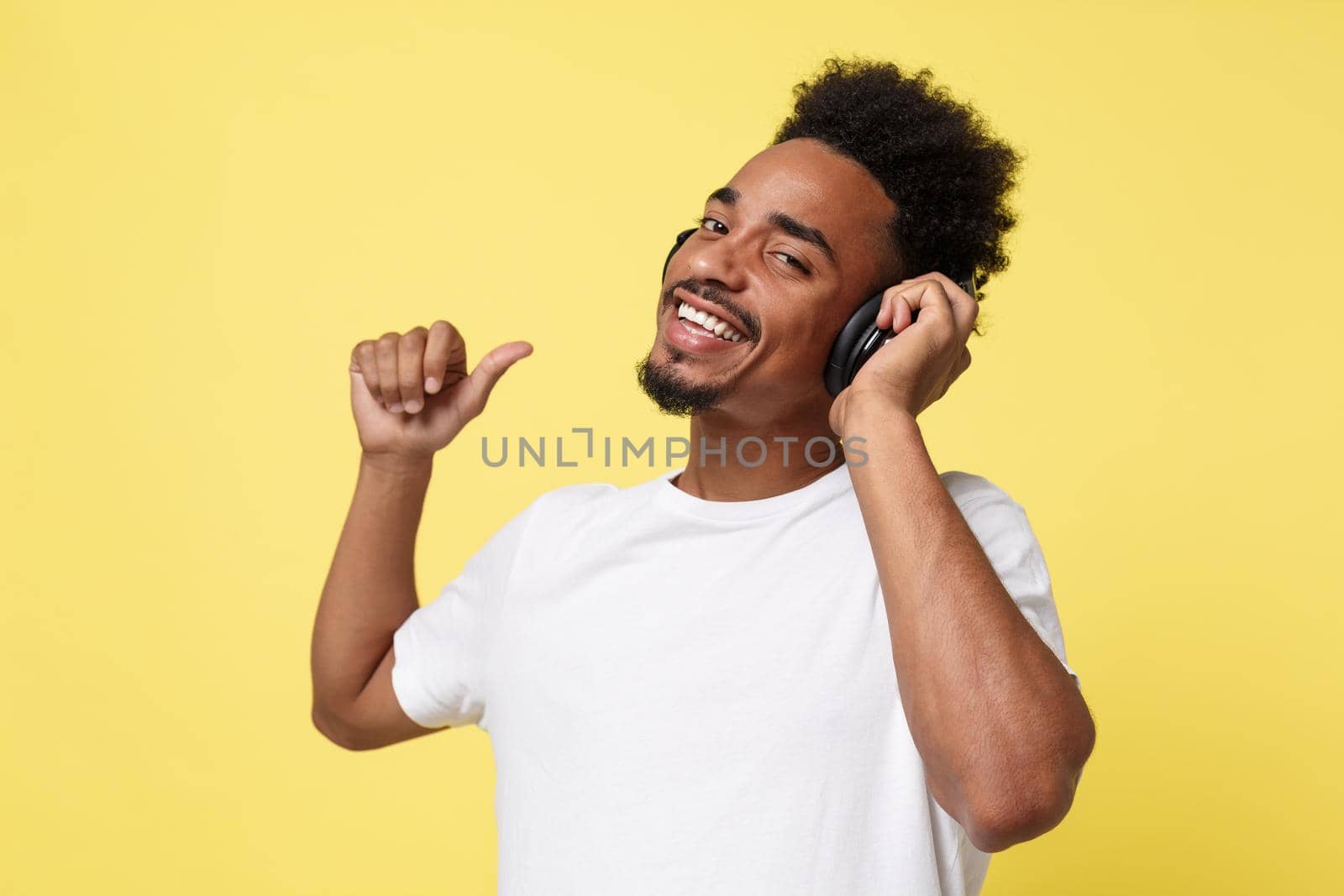 Attractive African American man with headphones listen to music. Isolated over yellow gold background. by Benzoix