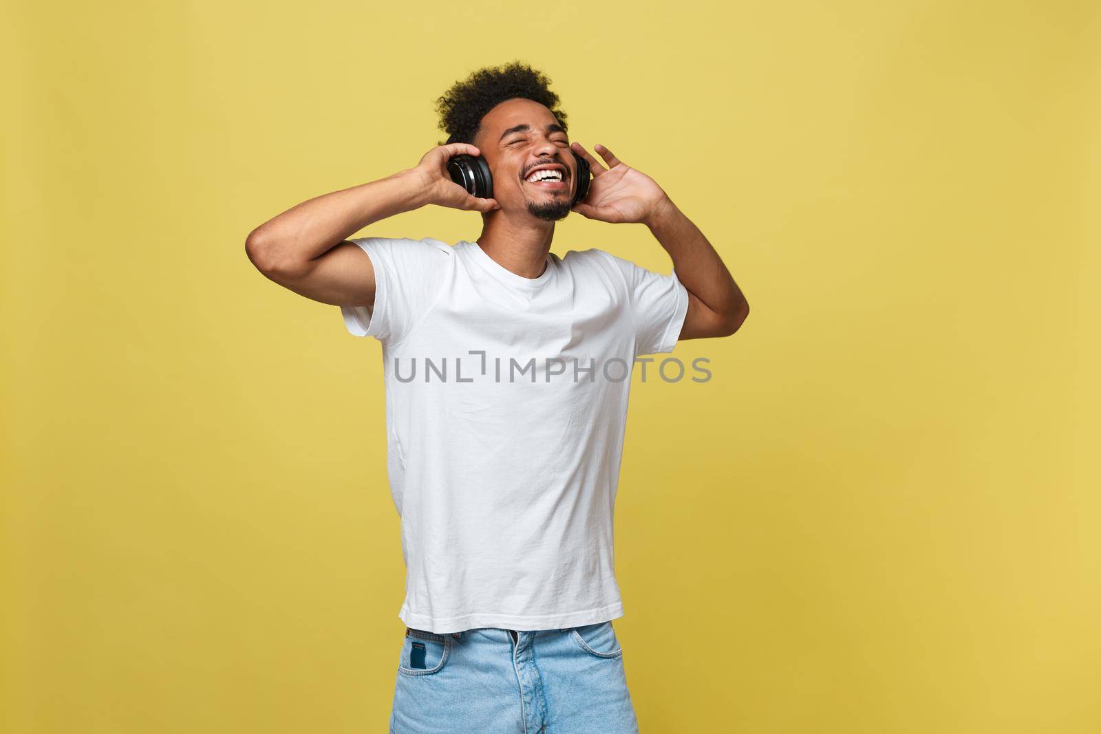 Young black man listening to music over his headphones. Isolated over yellow background
