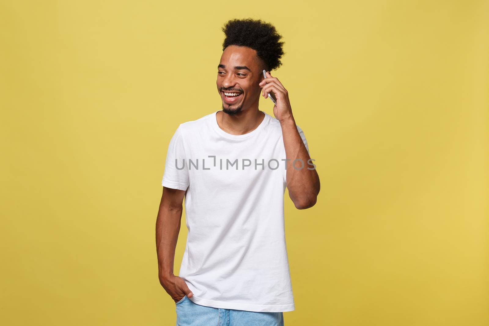 Young black man smiling and talking on mobile phone with copy space over yellow background