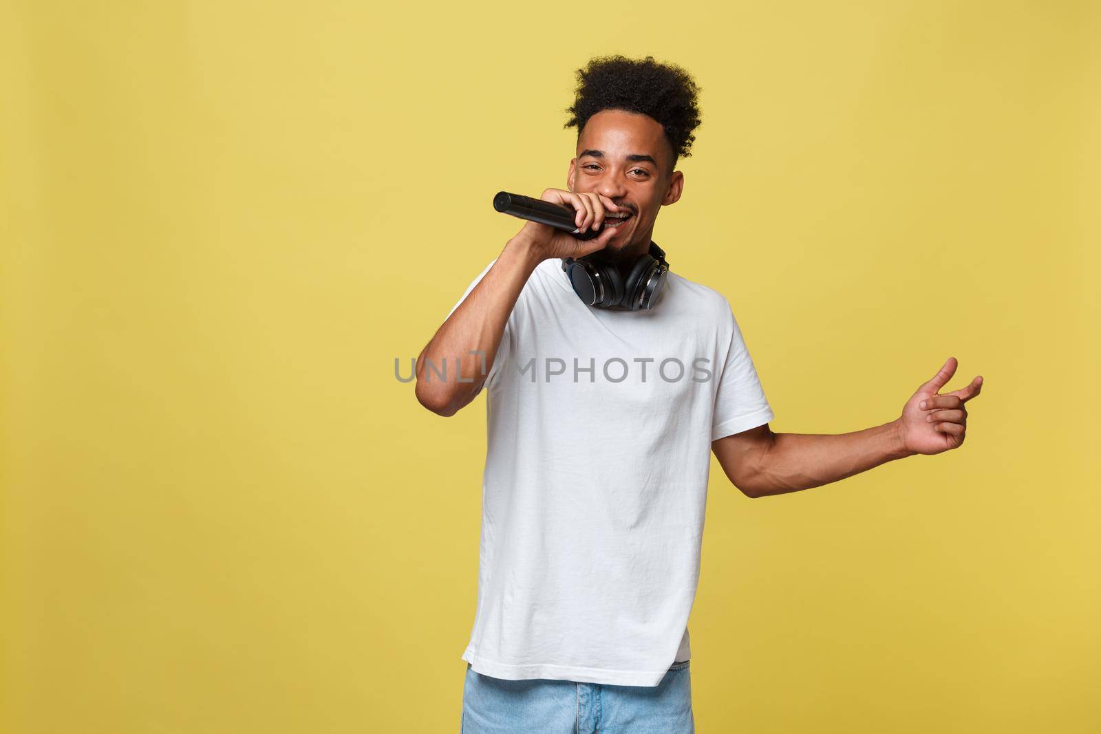 Young handsome African American Male Singer Performing with Microphone. Isolated over yellow gold background