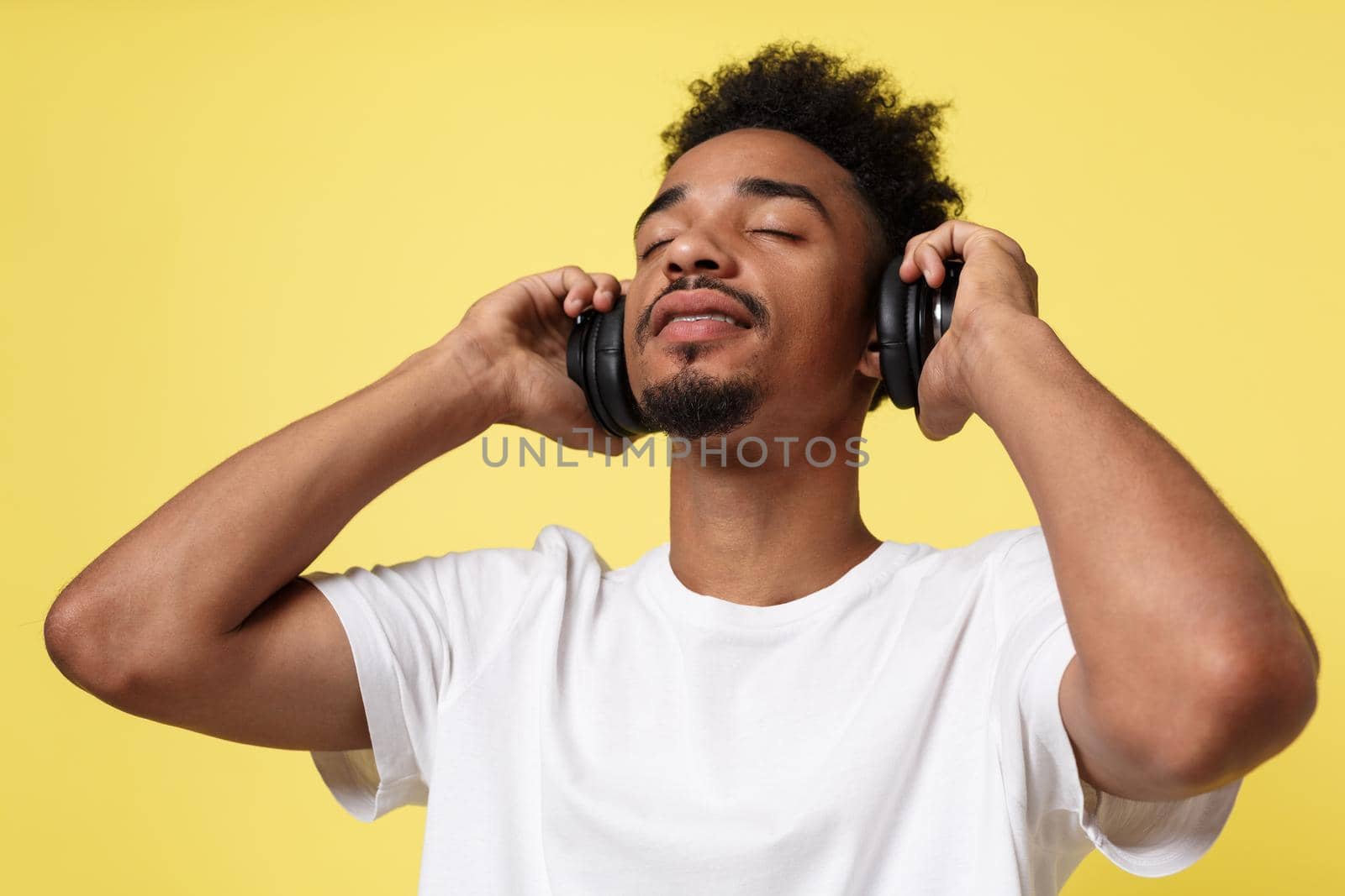 Attractive African American man with headphones listen to music. Isolated over yellow gold background