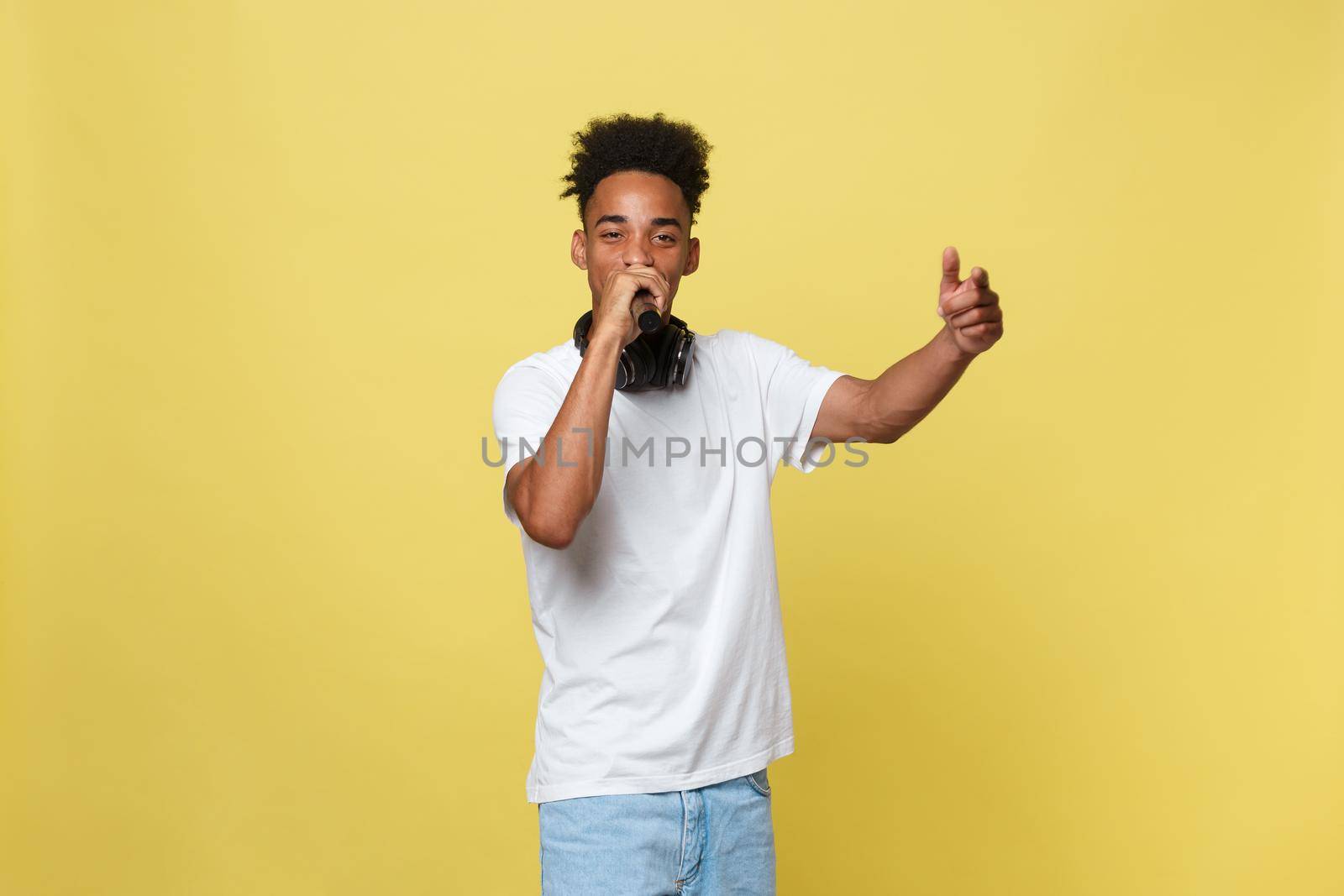 Attractive young dark-skinned man with afro haircut in white t shirt, gesticulating with hands and microphone, dancing and singing on party, having fun. by Benzoix
