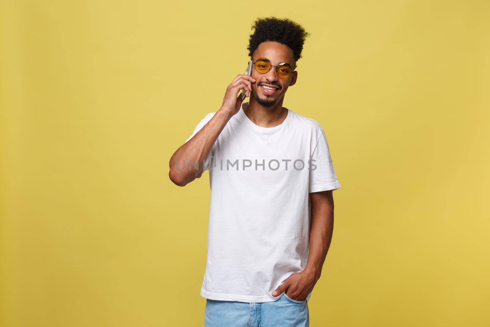 Portrait of cool young black guy talking on cellphone. Isolated on yellow background.