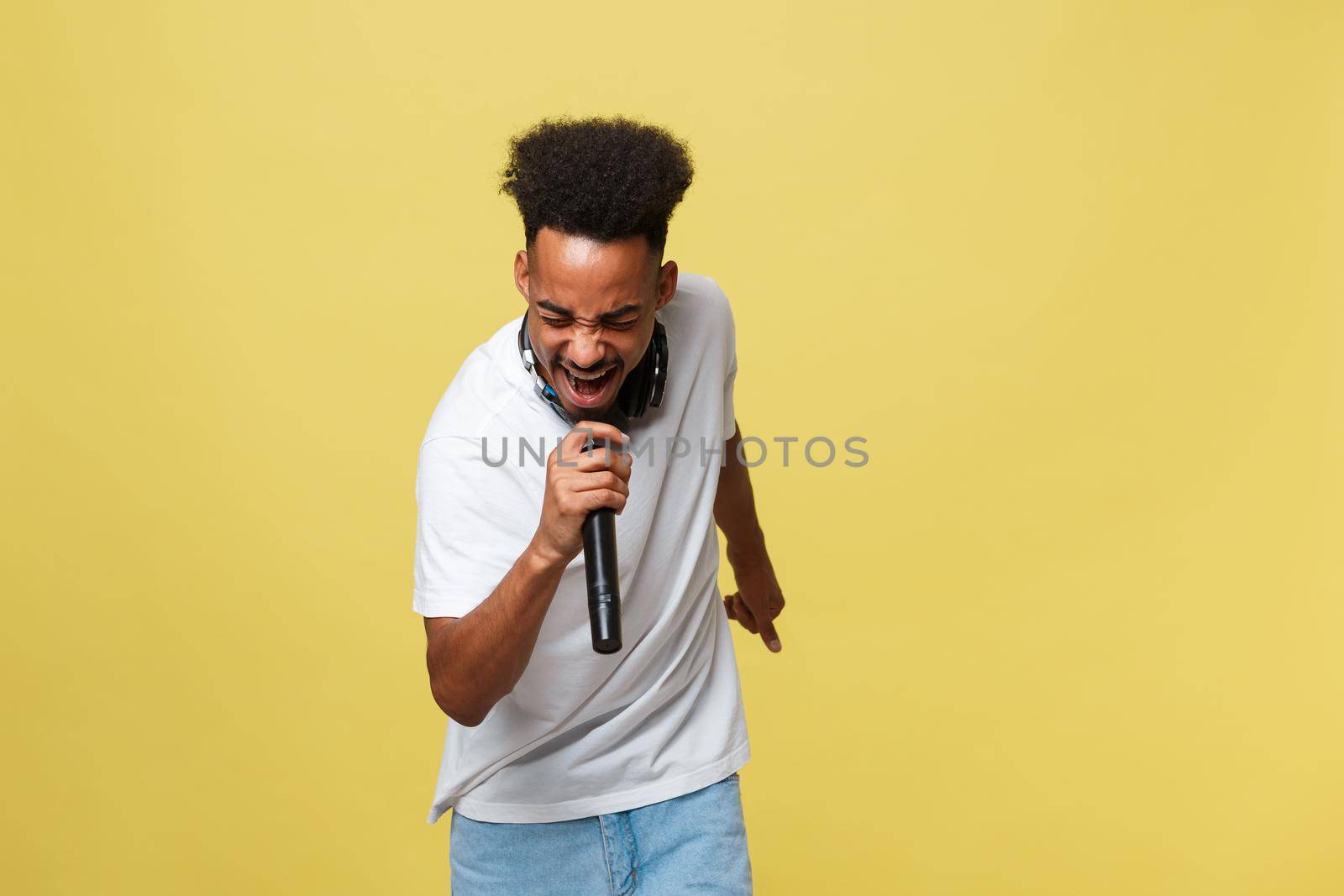 Young handsome African American Male Singer Performing with Microphone. Isolated over yellow gold background
