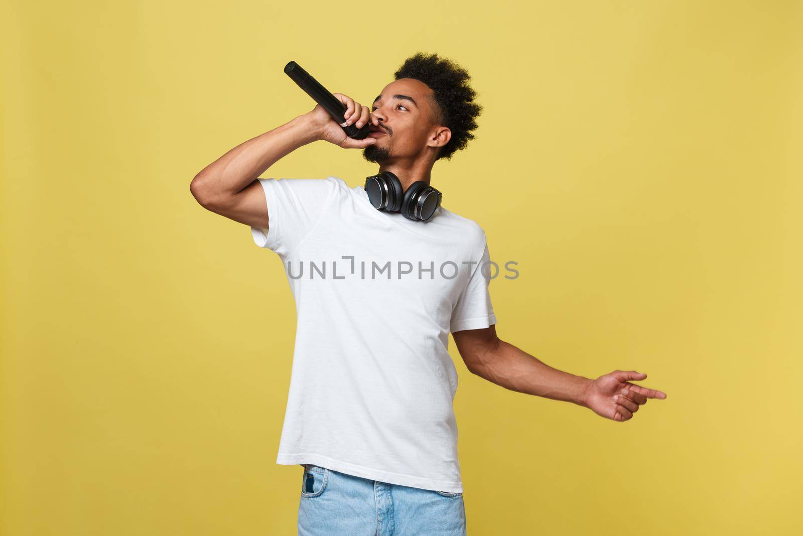 Young handsome African American Male Singer Performing with Microphone. Isolated over yellow gold background