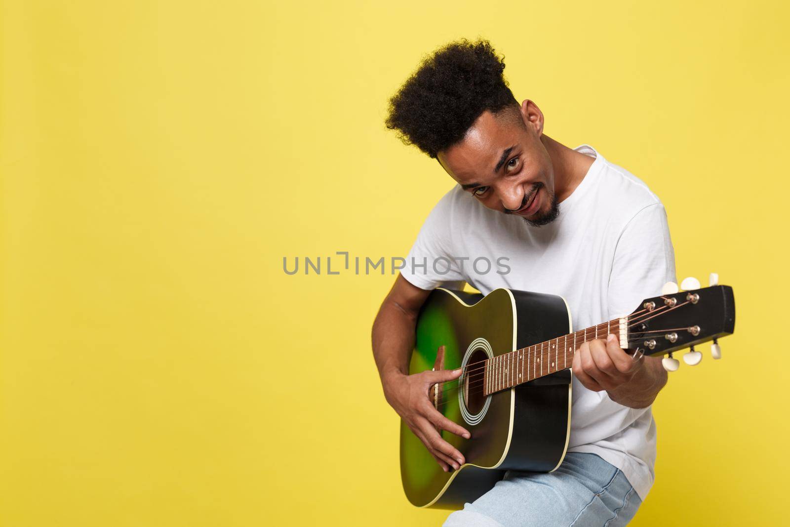 african american retro styled guitarist playing acoustic guitar isolated on yellow gold background.