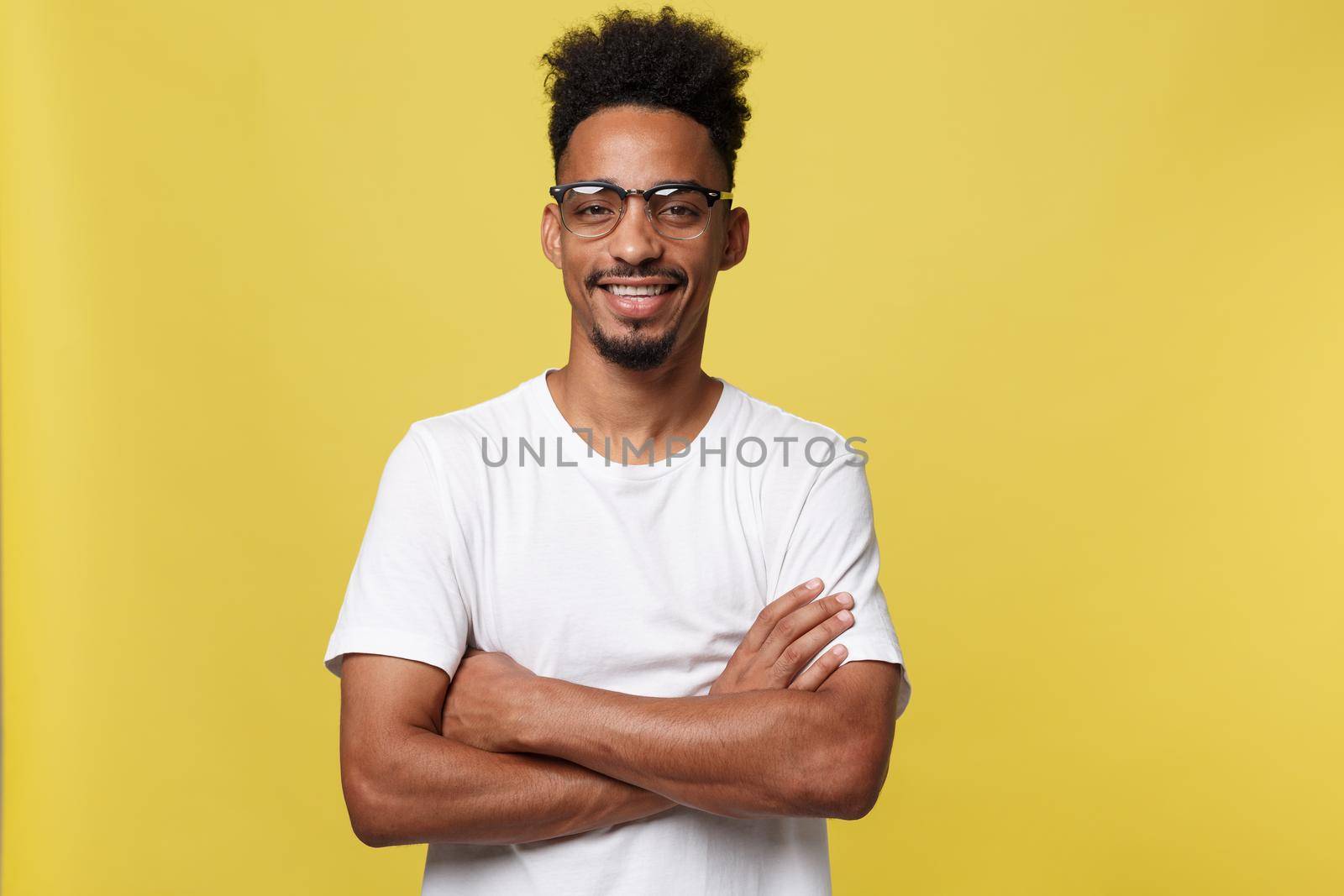 Close up portrait of a happy african american man posing with arms crossed on isolated yellow background.