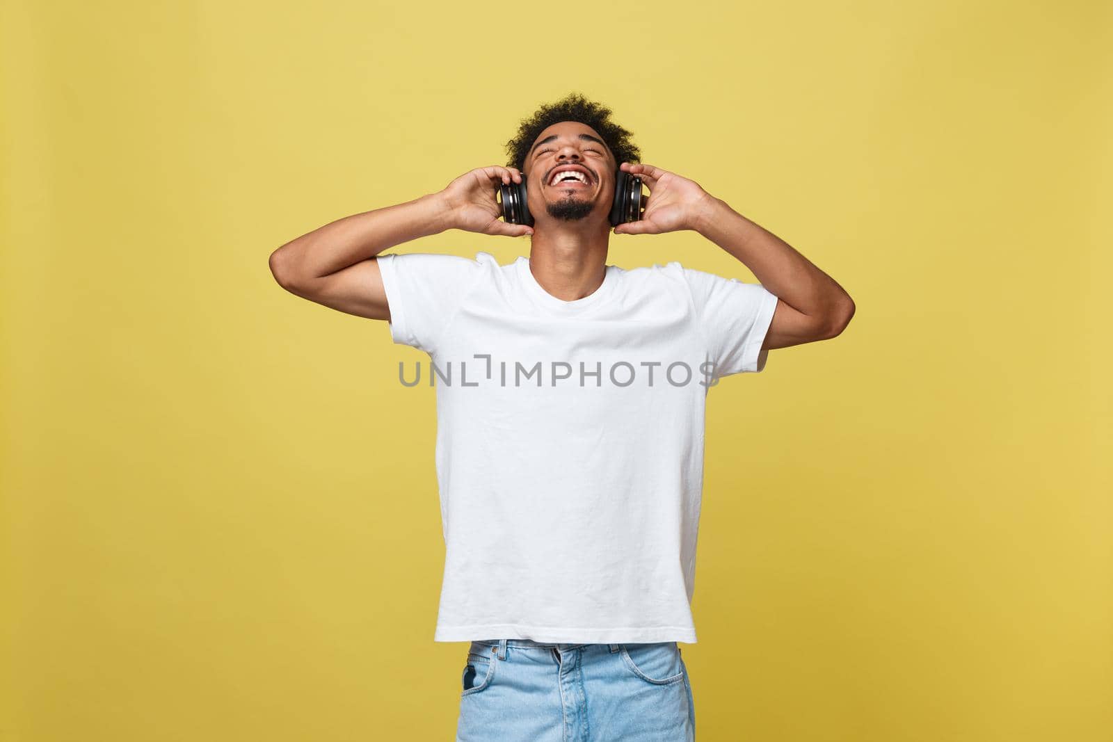 Young African American man wearing headphone and enjoy music over yellow gold Background.